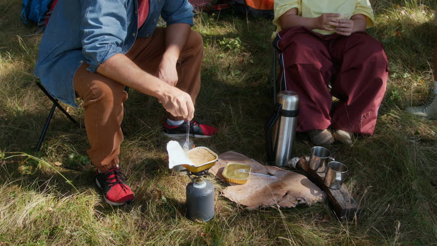 High angle shot tilt-up of man and young woman with down syndrome cooking food in camp while hiking in forest