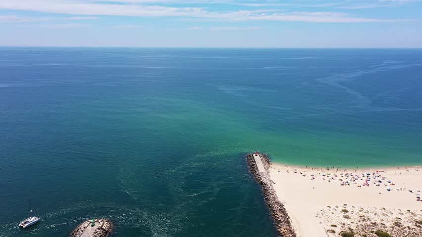 Aerial view drone shot of Tavira Portugal Algarve Aerial view jetty and water vivid turquoise and deep blue currents, small boat moored near sandbar, subtle algae swirls in channel, boater