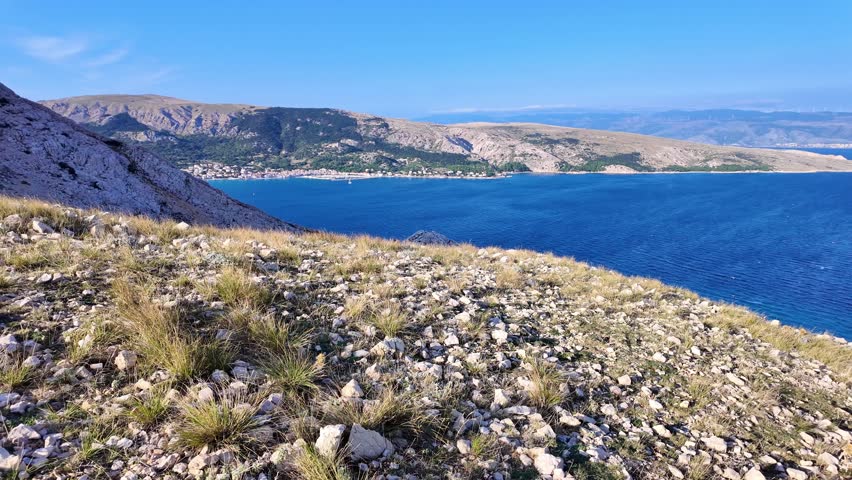 Majestic coastal landscape with rolling hills and vibrant blue sea under clear blue skies. Krk island, Croatia.
