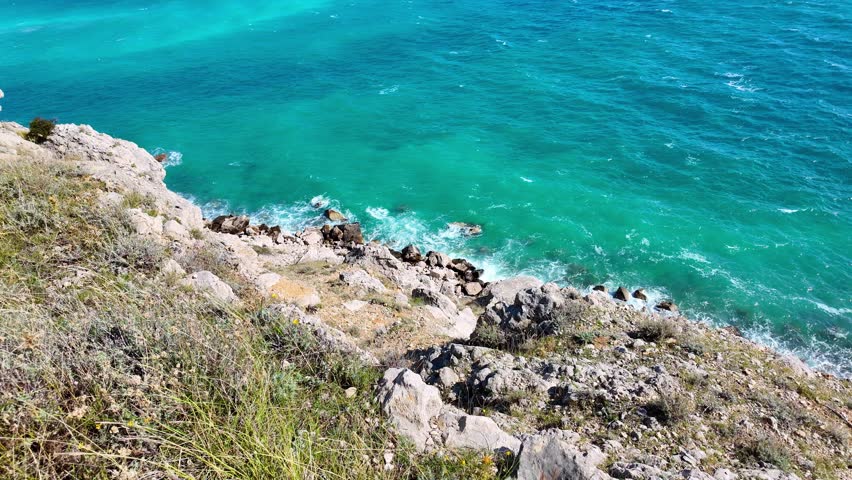 Coastal waves crashing on rocky shoreline amid vibrant turquoise waters.