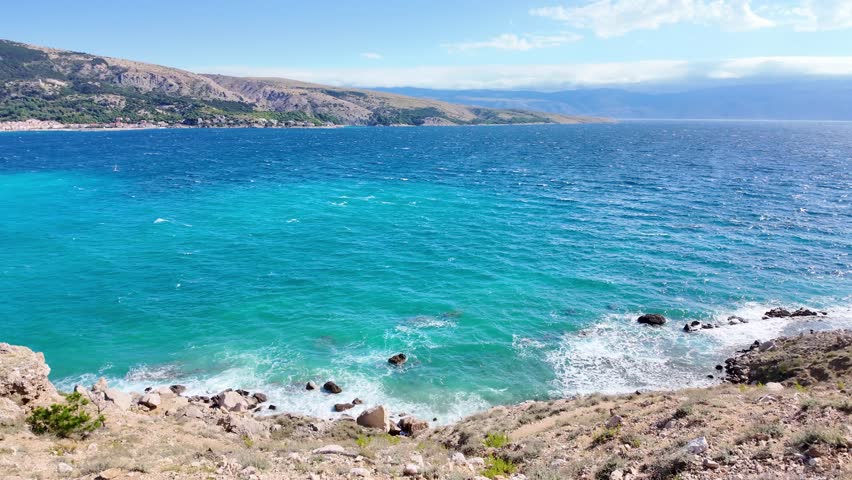 Majestic coastal waves crashing on rocky shore under clear blue sky.