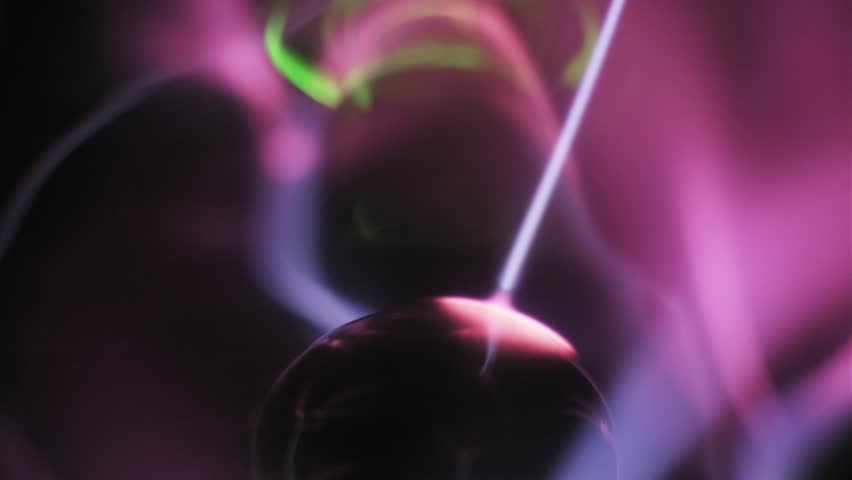 Extreme closeup of a central electrode emitting pink and purple plasma filaments. White electric arcs swirl through ionized gas streams with green light accents. Dark backdrop. High voltage current.