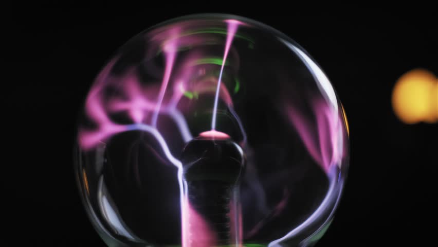 Side view plasma globe with pink purple electric currents moving from central coil to glass orb. Green neon light accents on dark background. High voltage energy experiment.