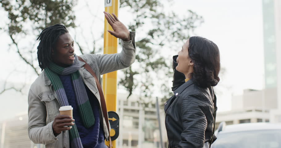 Diverse friends recognizing each other at bus stop pole, high-fiving, holding coffee and skateboard. Urban, casual, upbeat, friendship, community, contemporary, lifestyle