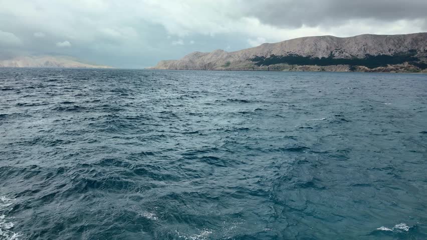 Dynamic coastal waves under cloudy sky with mountainous horizon.