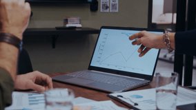 Close-up of business colleagues pointing at an investments trends graph on a laptop, discussing insights and smiling in agreement during a modern office meeting - Powered by Shutterstock - Get 15% off with code: PIKWIZARD15