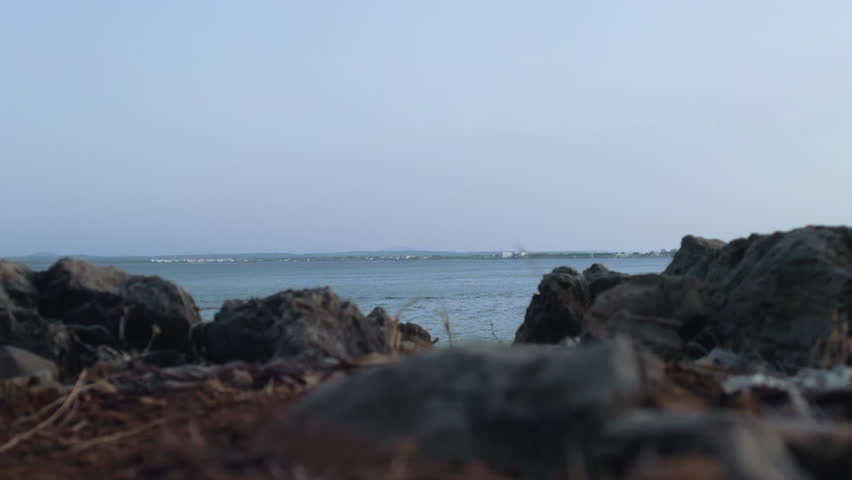 Rocks by the sea with distant horizon and pale blue sky