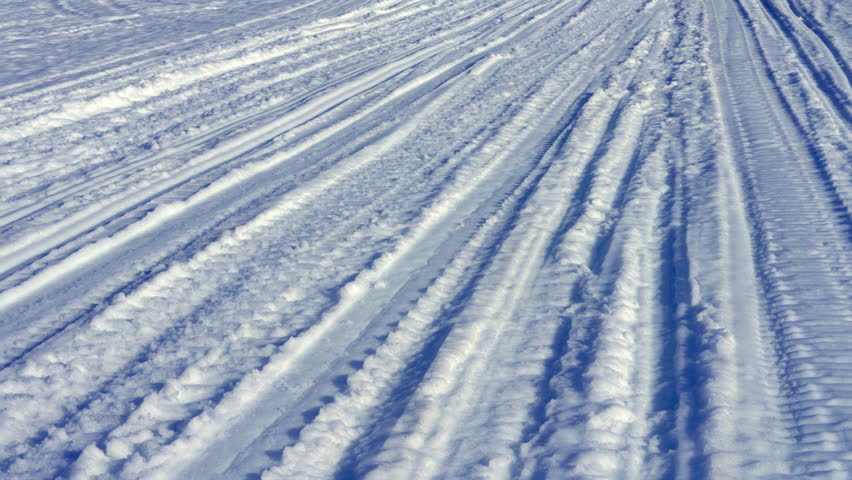 Snowmobile and ski tracks marking the fresh snow surface on a sunny winter day, creating a pattern of lines and shadows that lead into the distance on a pristine, cold landscape