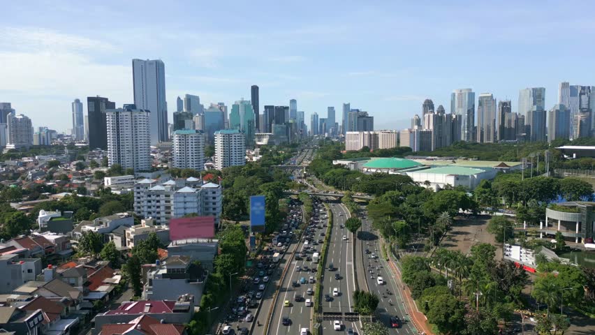 Aerial view of city traffic and modern skyline in Jakarta, Indonesia. Busy urban highway, tall skyscrapers, and green spaces in Southeast Asia