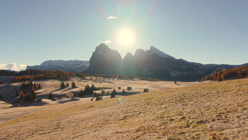 Aerial view of Alpe di Siusi or Seiser Alm during sunrise with wooden huts on autumn rolling hill and trees in Dolomites, Italy