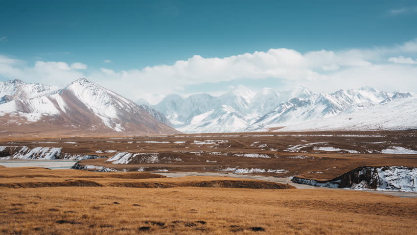 Scenic timelapse landscape of Sary Jaz remote valley with Tian Shan mountain range with snow covered and clouds in blue sky on golden wilderness at Kyrgyzstan