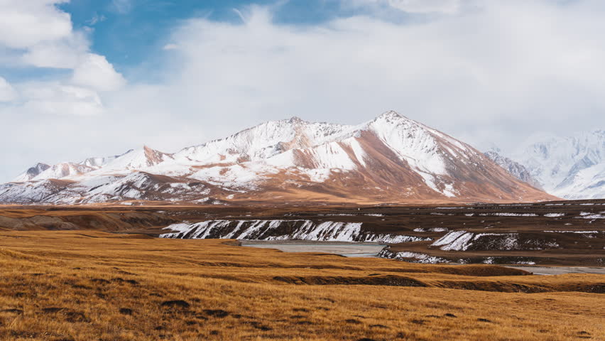 Scenic timelapse landscape of Sary Jaz remote valley with Tian Shan mountain range with snow covered and clouds in blue sky on golden wilderness at Kyrgyzstan