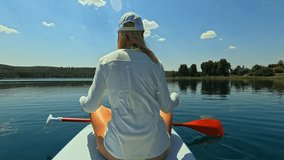 Young blonde woman from behind sitting on stand up paddleboard in middle of calm lake, meditating in lotus yoga pose on sunny day with blue sky and some white clouds - Powered by Shutterstock - Get 15% off with code: PIKWIZARD15