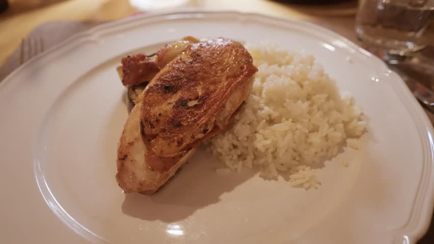 Close-up view of a grilled chicken breast served with white rice on a restaurant plate