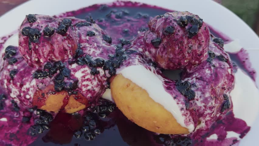 Close-up shot of fried doughnuts topped with sour cream and blueberry jam, slow movement, served as a traditional Romanian dessert in restaurant setting
