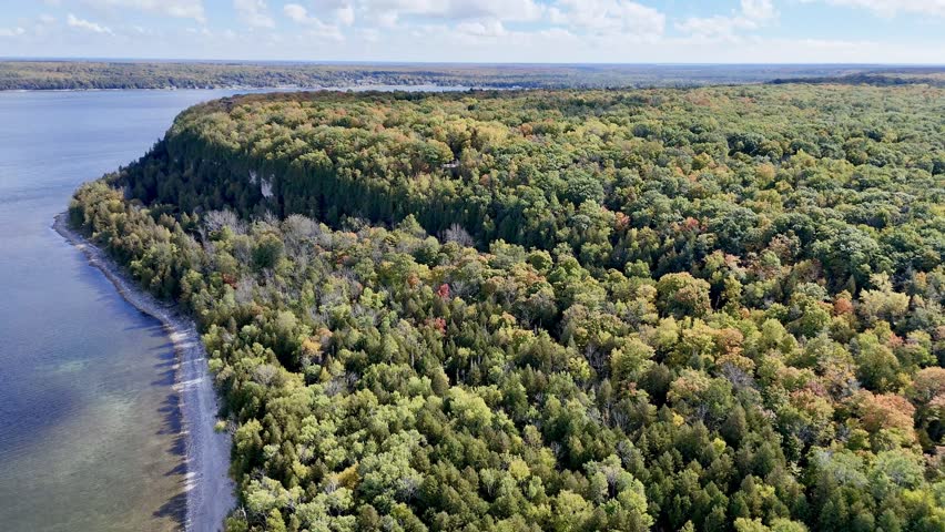 Aerial video of vibrant autumn foliage in Peninsula State Park as a drone glides toward scenic Ephraim Harbor in Door County, Wisconsin