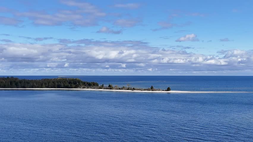 Aerial video of a drone flying from Jackson Harbor over clear turquoise waters toward Washington Island, revealing forested shores, boats, and the scenic meeting of Lake Michigan and Green Bay