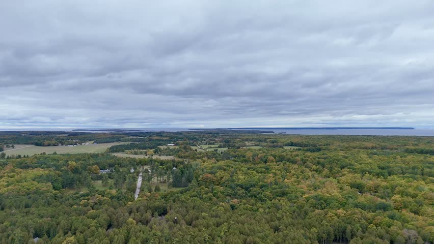Aerial panoramic video of Schoolhouse Beach on Washington Island, showcasing turquoise waters, smooth white stones, and vibrant autumn foliage along the wooded shoreline.