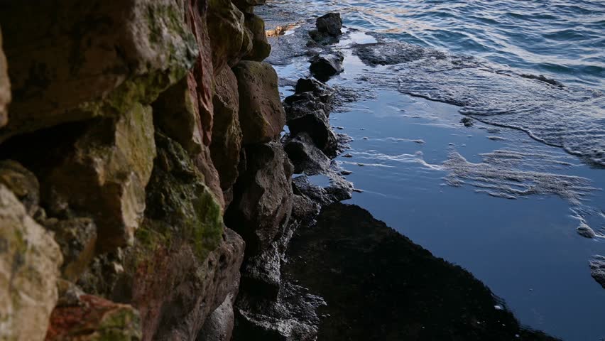 Polignano a Mare, Italy, Small sea waves hitting the rocky shore of a sea cave, a rocky cliff