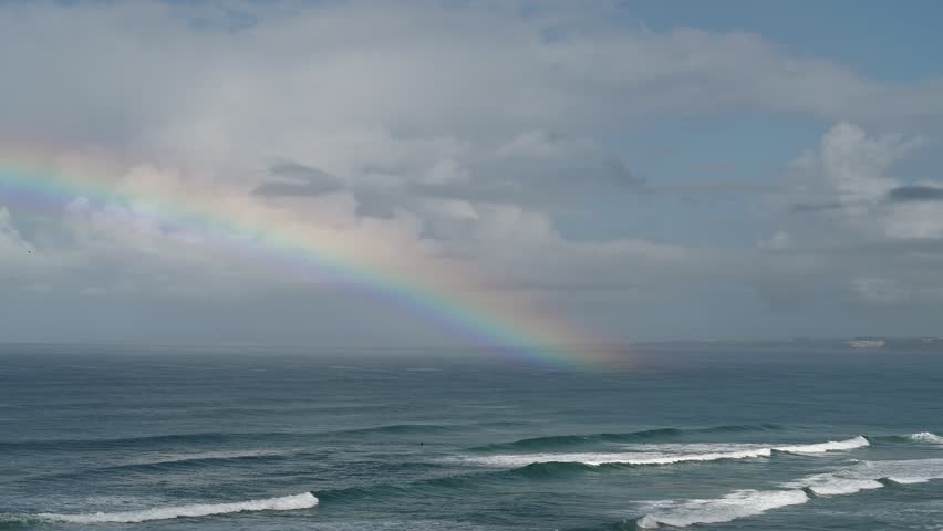Rainbow stretching over the Atlantic Ocean above sandy beach in Santa Cruz Portugal

