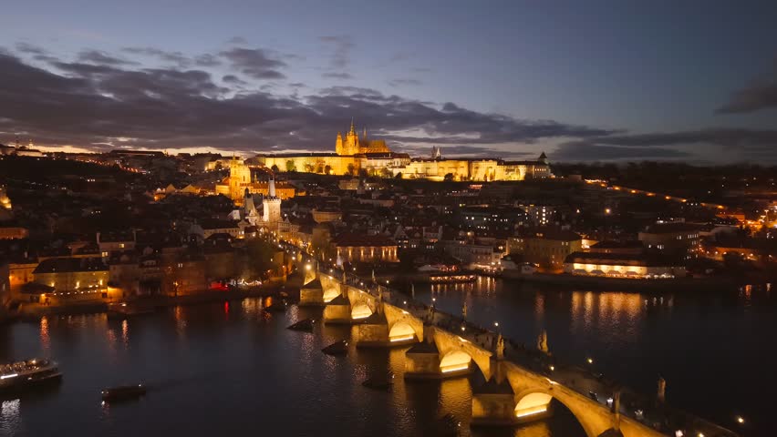 Experience the breathtaking beauty of Prague as the city illuminates during dusk. The Vltava River reflects the lights near the historic bridges and the castle skyline.