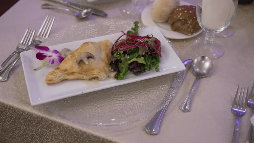 A plated appetizer with puff pastry and salad on a formal dining table. The elegant setting evokes a gourmet experience at a wedding or banquet. Ideal for culinary and event content.