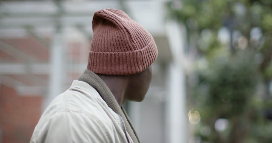 African American man outdoors hearing sound and turning toward camera, pausing, walking, copy space. Urban, candid, contemplative, casual, scenic, introspective, moody