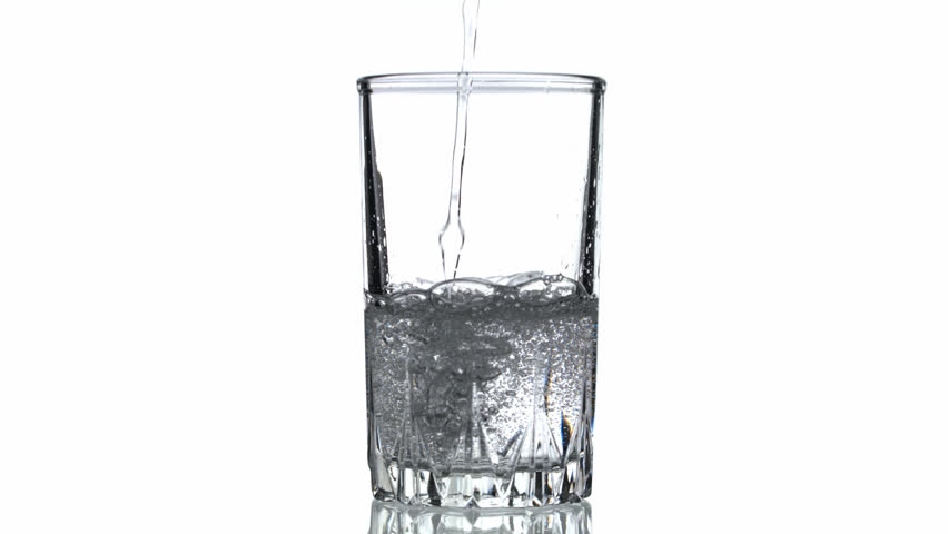 A glass of water is being poured into it. The water is clear and the glass is half full