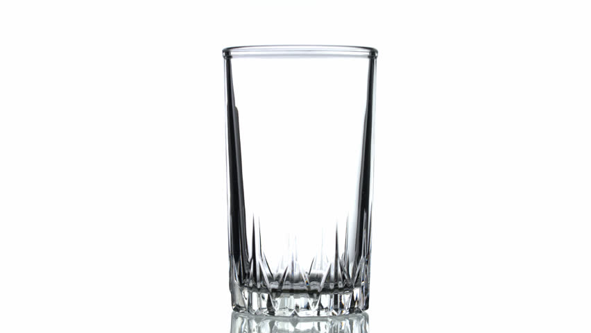 A glass of water is being poured into it. The water is clear and the glass is half full