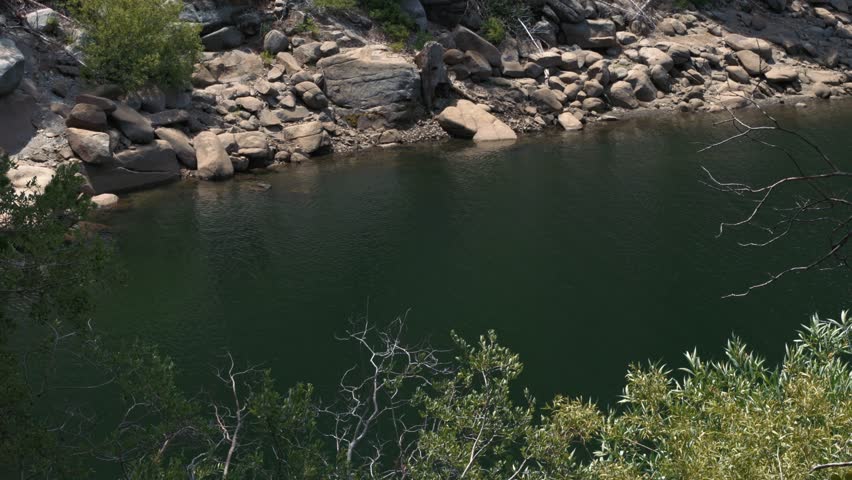 Rocky shore of mountain lake with green trees
