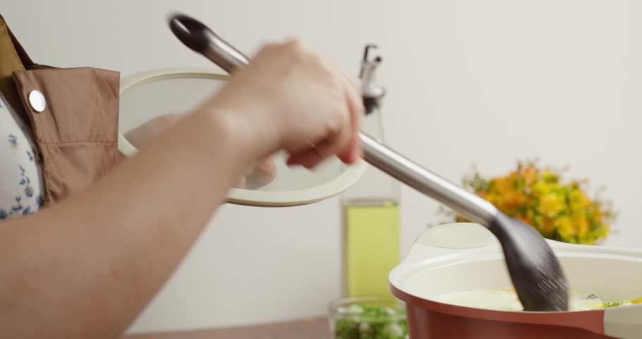 A woman prepares broccoli soup and adds it, stirs it with a ladle and covers the pot with a lid. Creamy broccoli soup with vegetables, boiling in a saucepan.