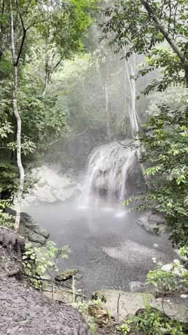 Aguas Calientes waterfall in El Estor, Izabal, Guatemala, flowing into a clear natural pool surrounded by lush tropical forest and light mist, creating a calm and peaceful nature scene.