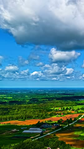A Scenic Countryside With Fields and Farms Lies Under a Bright Blue Sky Filled With Fluffy Clouds - Vertical Hyperlapse Shot