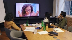 Diverse coworkers in modern office attending online meeting with female colleague on screen showing teamwork communication and collaboration during corporate video conference call - Powered by Shutterstock - Get 15% off with code: PIKWIZARD15
