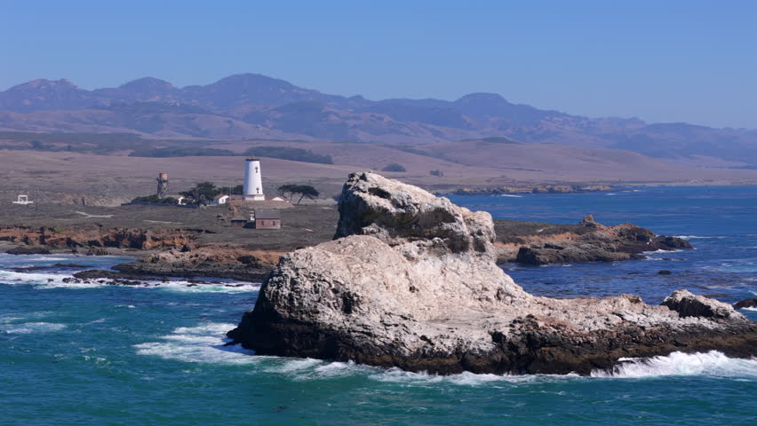 Aerial drone view of Point San Luis Lighthouse near Avila Beach California with rocky shoreline, deep blue ocean water and distant hills captured from a high angle for scenic travel and nature themes