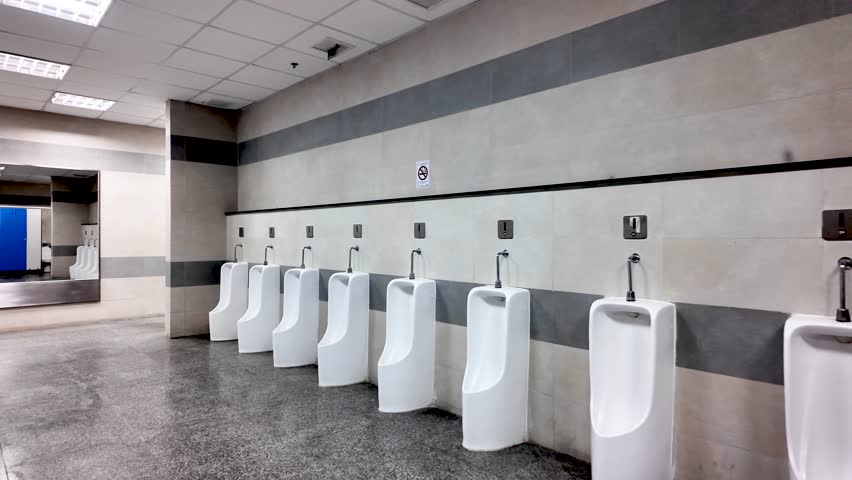 Row of clean white urinal bowls lining a gray and white wall in a public men