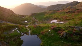 Rodnei mountains, Romania. Stunning aerial wide shot of a pristine alpine valley campsite with colorful tents, winding stream, small lake, and patches of snow, illuminated by a warm sunrise. - Powered by Shutterstock - Get 15% off with code: PIKWIZARD15