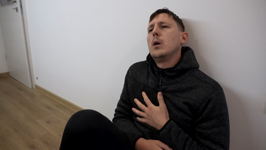 Young caucasian man sits indoors against wall struggling with crippling anxiety