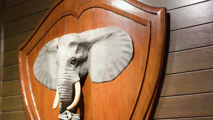 Wooden elephant head sculpture on wall, warm indoor lighting, slow camera pan, traditional Thai decor