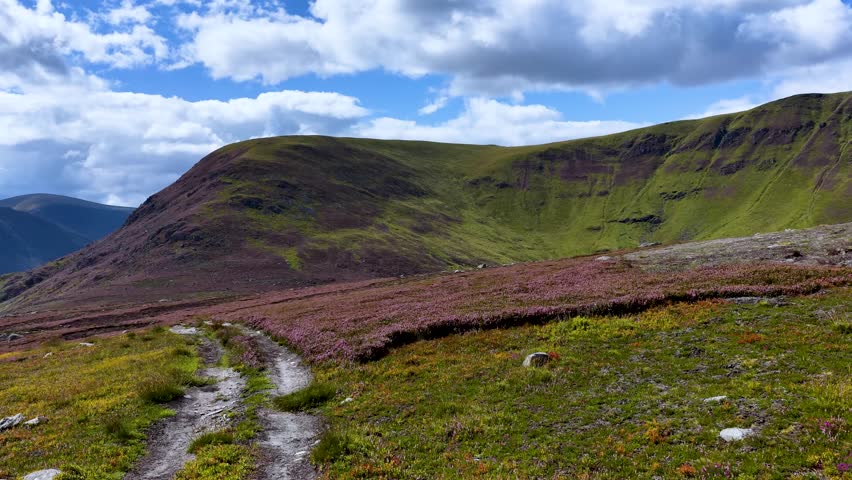 Wide daylight pan reveals green hills, rugged terrain, and dramatic clouds in Scottish Highlands