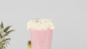 Hand places cherry on whipped cream-topped pink smoothie in bright studio with fruit background - Powered by Shutterstock - Get 15% off with code: PIKWIZARD15