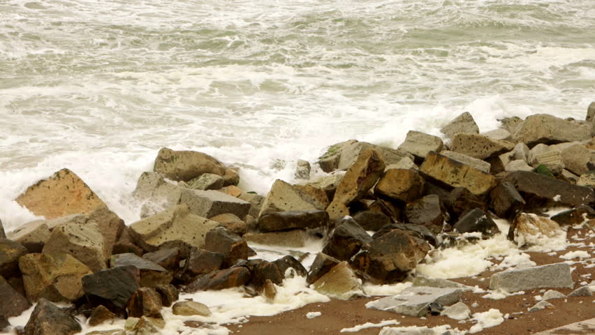 Static shot of waves crashing against large coastal rocks at the shoreline in Japan on an overcast day