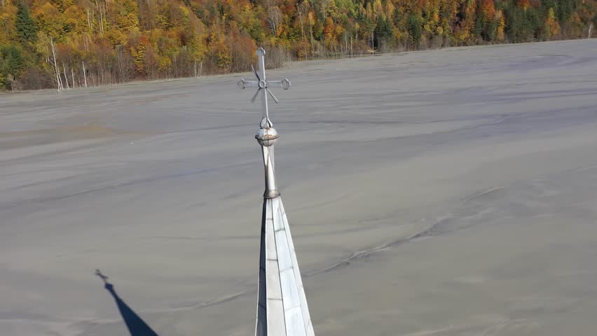  Aerial slow motion view of a church tower with cross, buried under mud in decanting lake