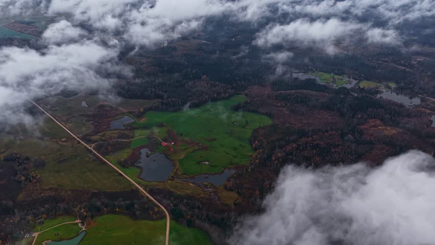 Clouds Drift Over Fields and Forests, Revealing Glimpses of the Land Below - Aerial Drone Shot
