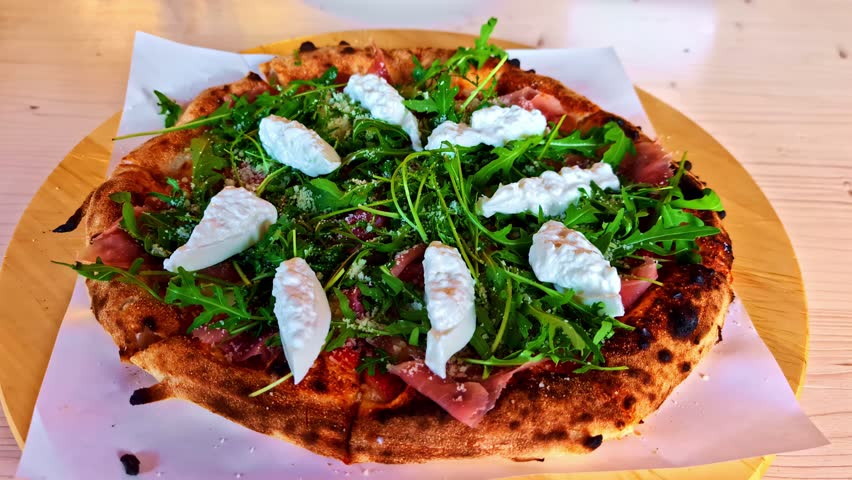 Wood-fired pizza topped with prosciutto, arugula, and dollops of burrata cheese