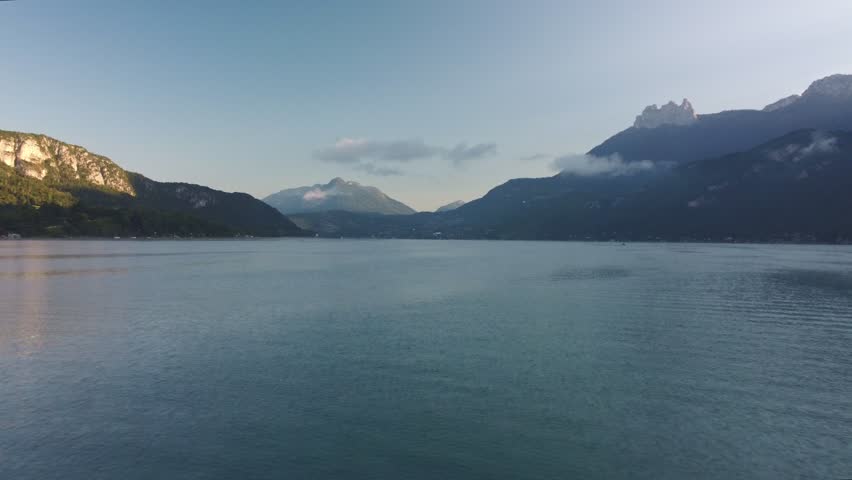 Lake Annecy, France on a bright morning. Just after the sun appears over the surrounding mountains aerial footage flies backwards revealing the amazing surroundings and mountains.