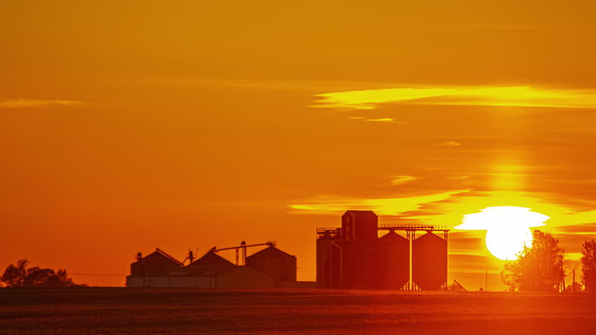 Golden sunrise behind grain silos and farm buildings on open countryside farmland