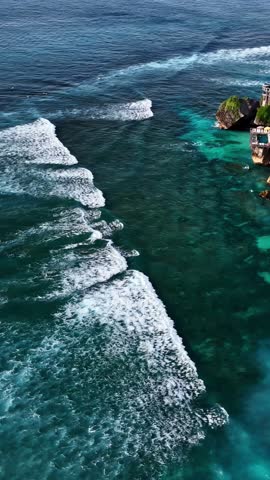 Drone of Uluwatu coastal resorts above clear blue water and surfers near rocky cliff shoreline