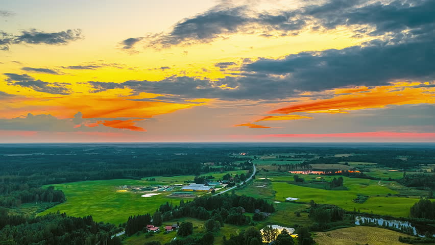 Aerial timelapse of glowing fire sunset sky above farmlands along highway edge