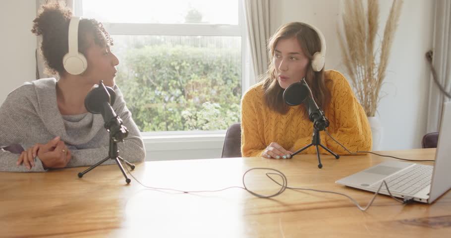 Diverse female co-hosts alternating speaking and listening at table with mics for podcasting. Collaboration, communication, discussion, professional, creative, modern, conversational